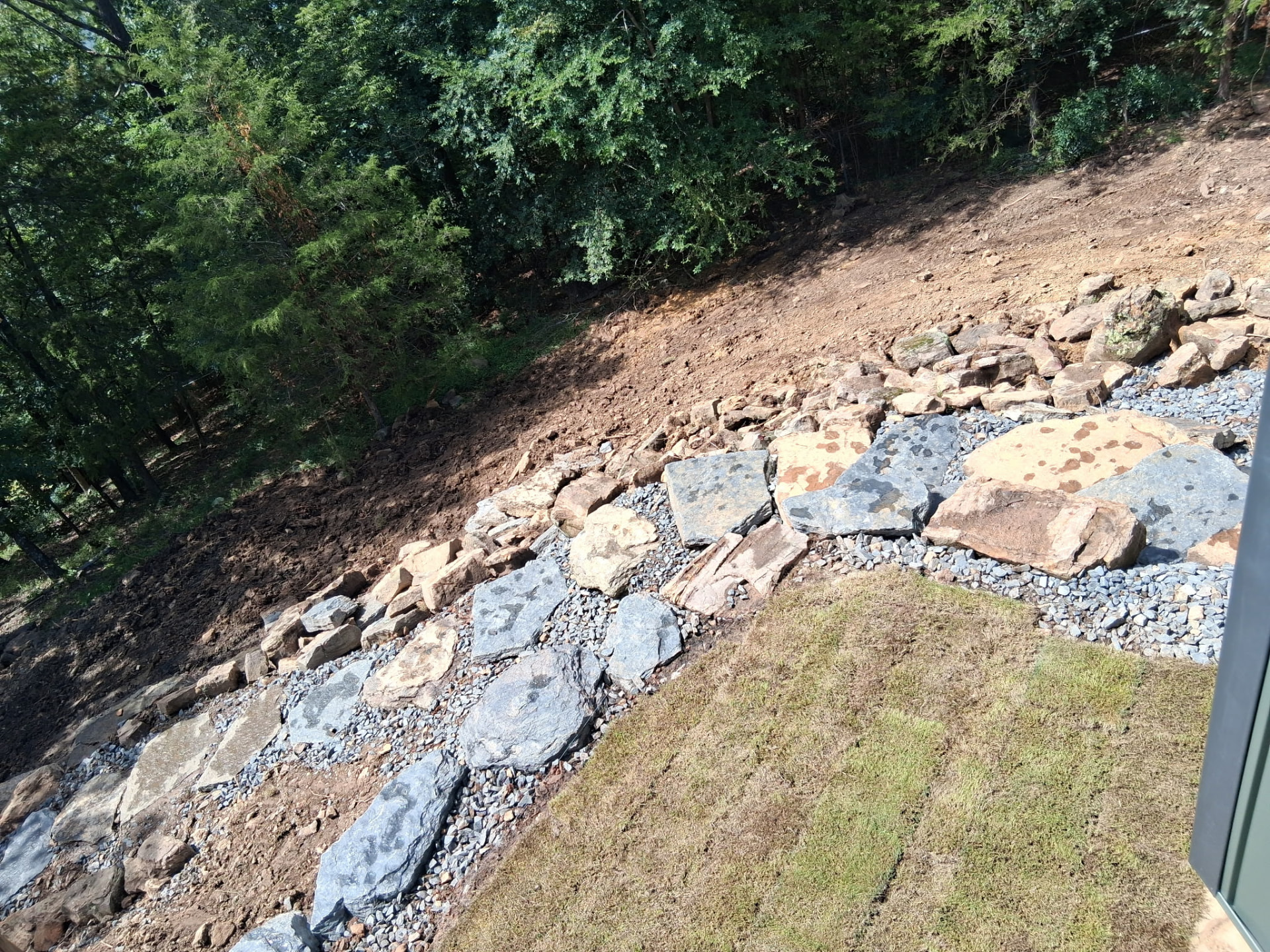 Graded hillside with stepping stones, rock-lined drainage and new sod after landscaping in Heber Springs, Arkansas